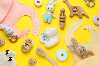 Flat lay composition with silicone baby bibs, toys and accessories on yellow background