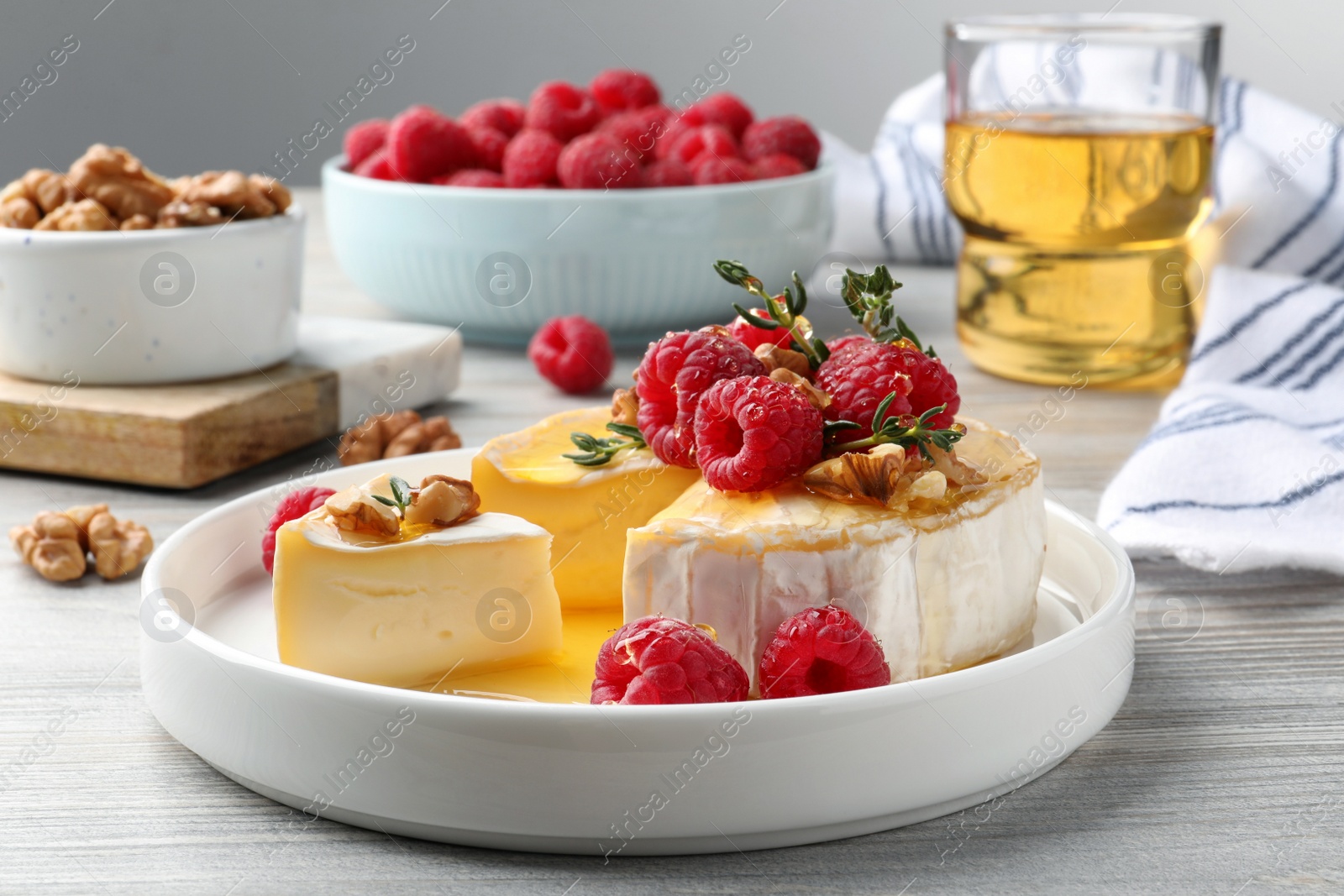 Photo of Brie cheese served with raspberries, walnuts and honey on white wooden table