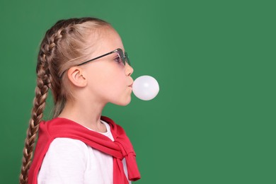 Photo of Girl in sunglasses blowing bubble gum on green background, space for text