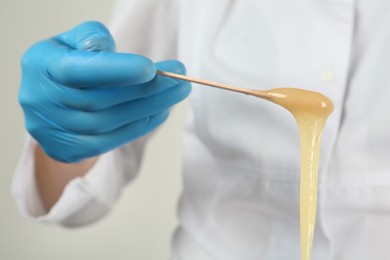 Woman in gloves holding spatula with hot depilatory wax, closeup