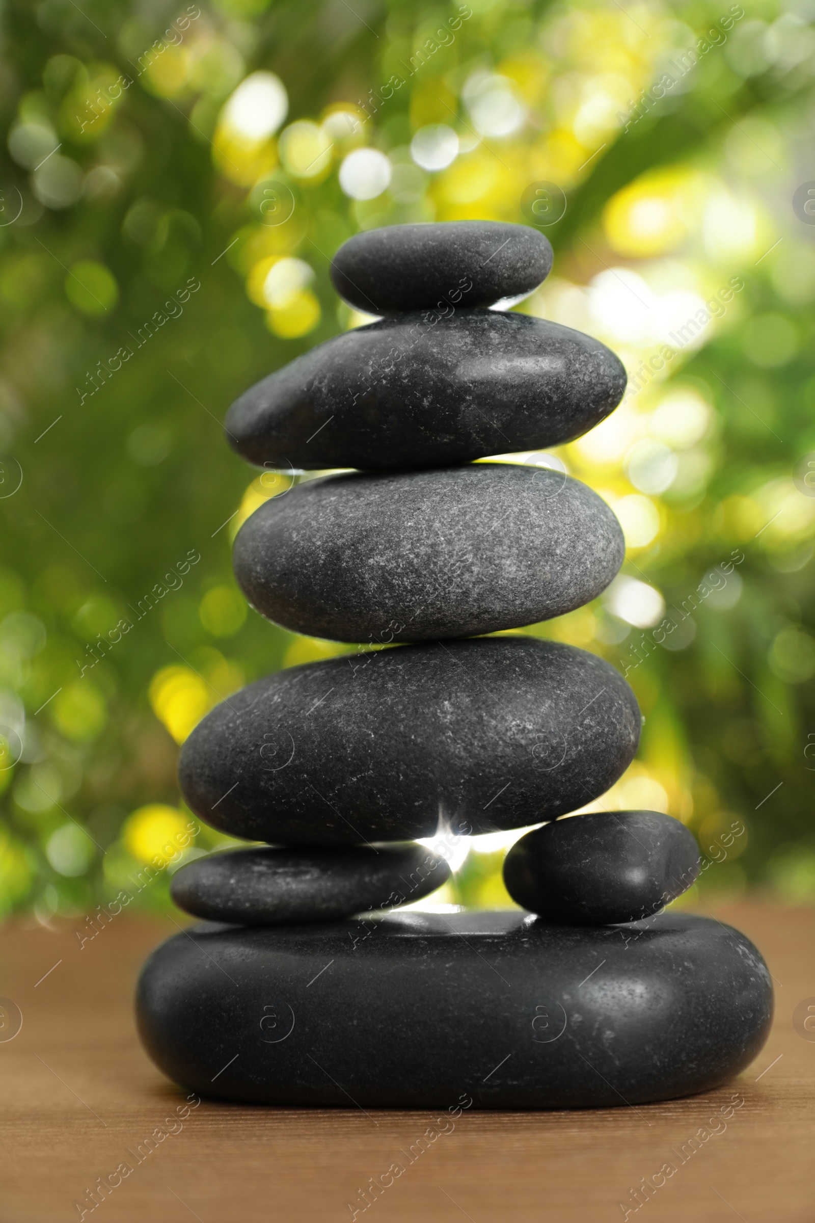 Photo of Stack of stones on wooden table against blurred green background, closeup. Zen concept