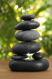 Stack of stones on wooden table against blurred green background, closeup. Zen concept