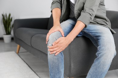 Photo of Man suffering from knee pain at home, closeup. Space for text