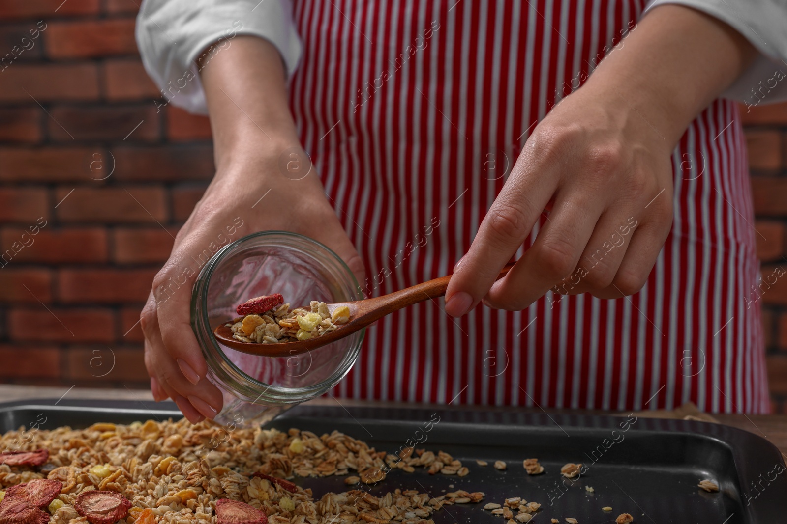 Photo of Woman putting granola from baking tray into jar at table, closeup