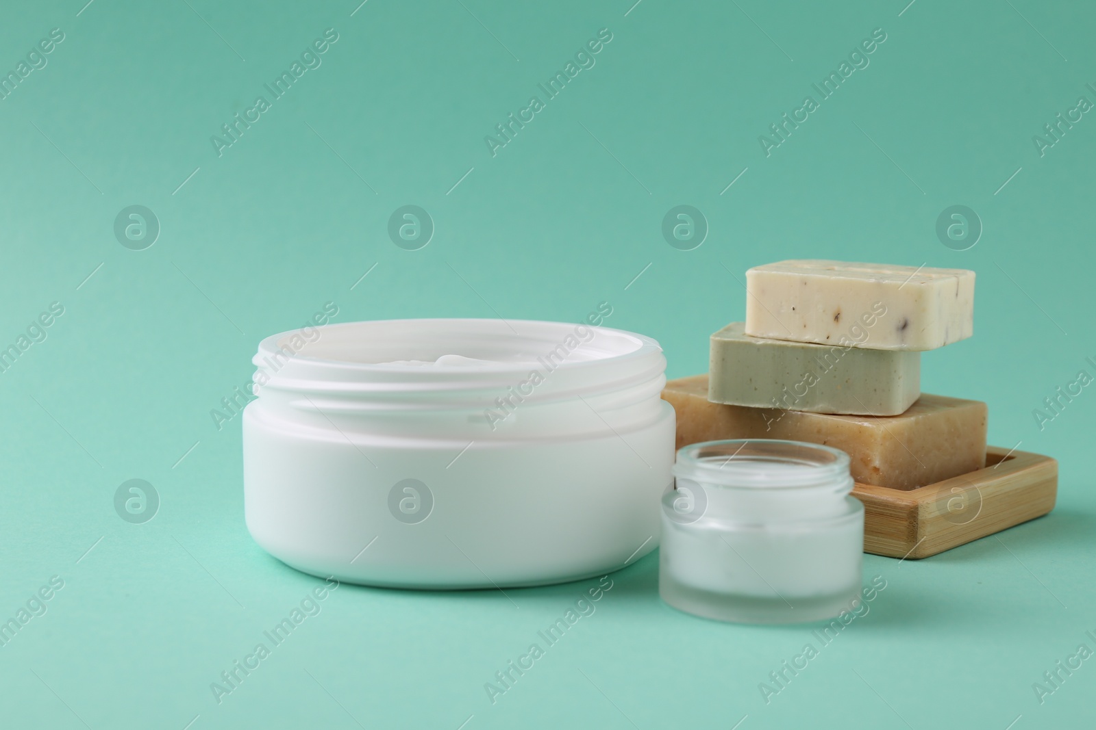 Photo of Moisturizing cream in open jars and soap bars on turquoise background. Body care products