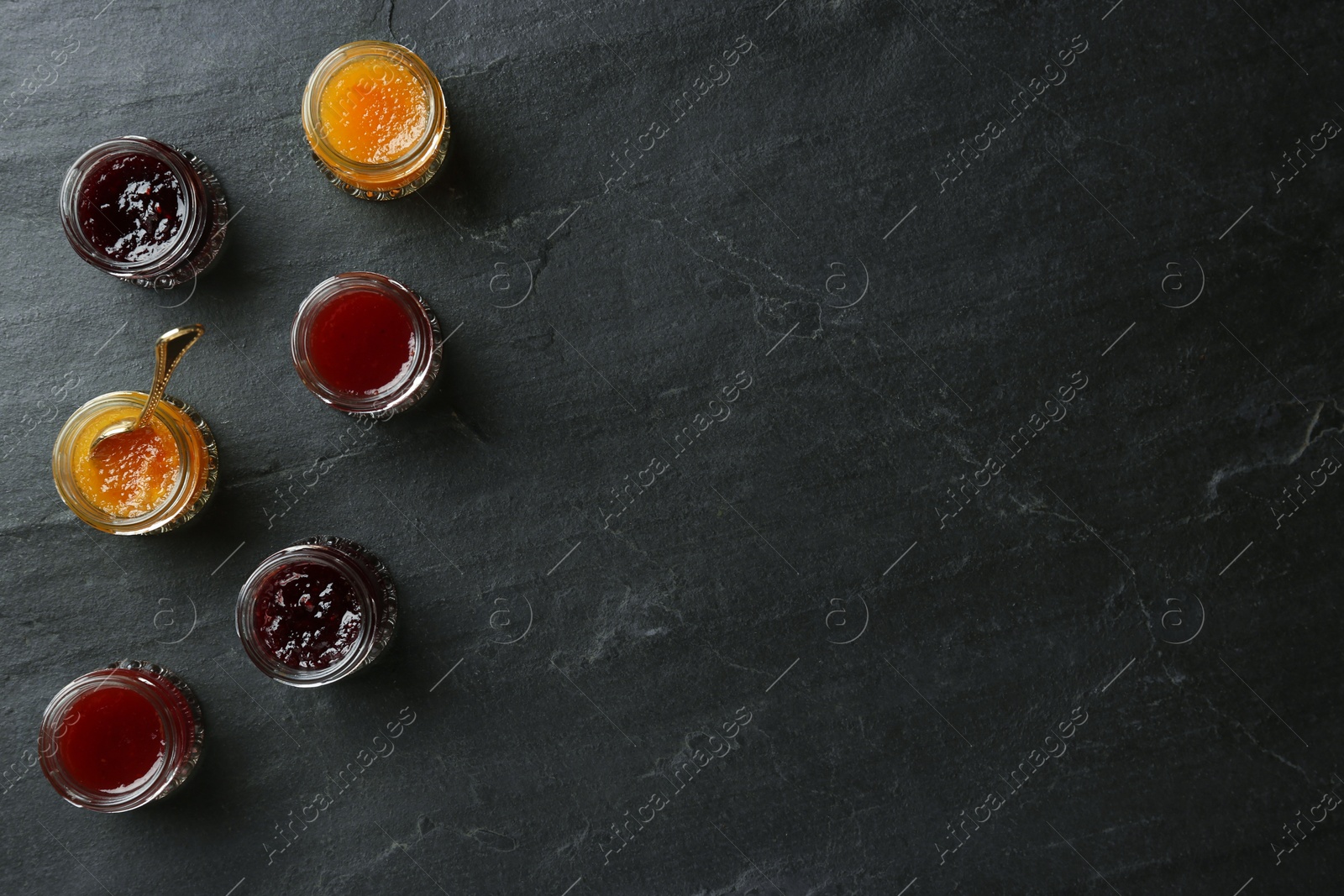 Photo of Jars of different jams on black table, flat lay. Space for text