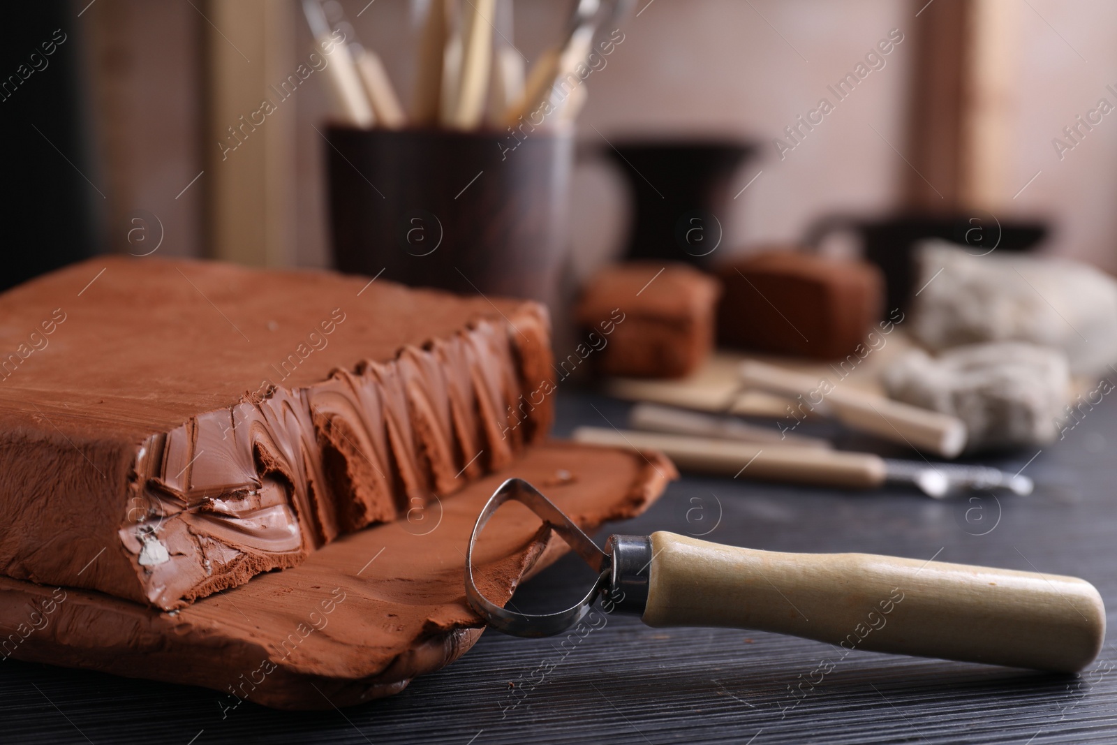 Photo of Clay and loop tool on dark gray wooden table in workshop, closeup