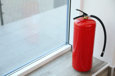 Photo of Fire extinguisher near window indoors. Space for text