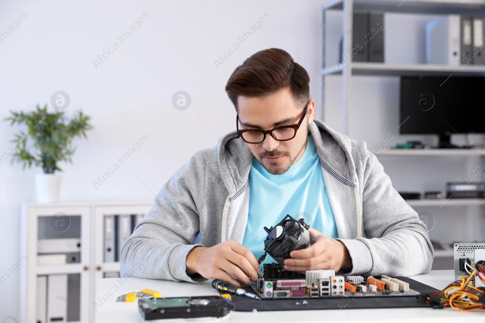 Photo of Male technician repairing motherboard at table indoors