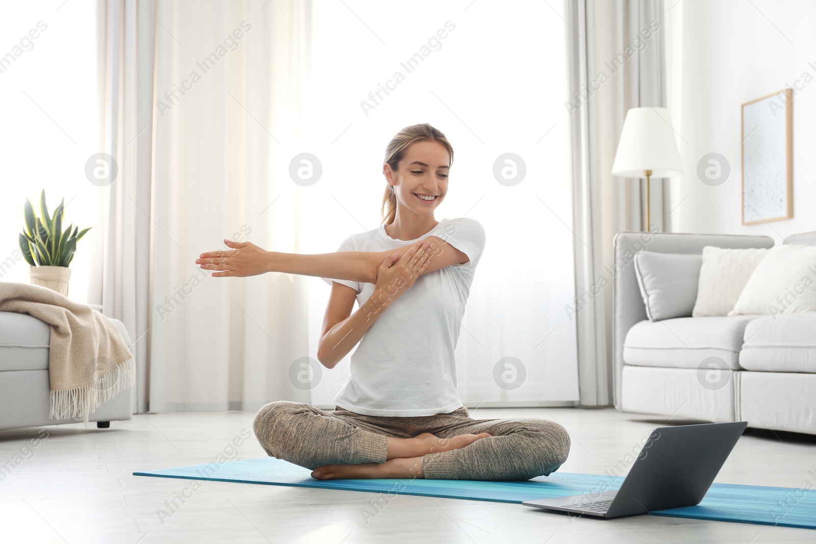 Photo of Woman having online video class via laptop at home. Distance yoga course during coronavirus pandemic