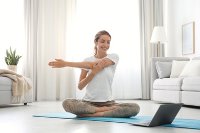 Photo of Woman having online video class via laptop at home. Distance yoga course during coronavirus pandemic