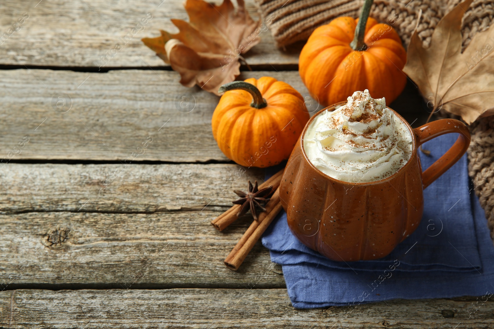 Photo of Mug of pumpkin spice latte with whipped cream and ingredients on wooden table. Space for text