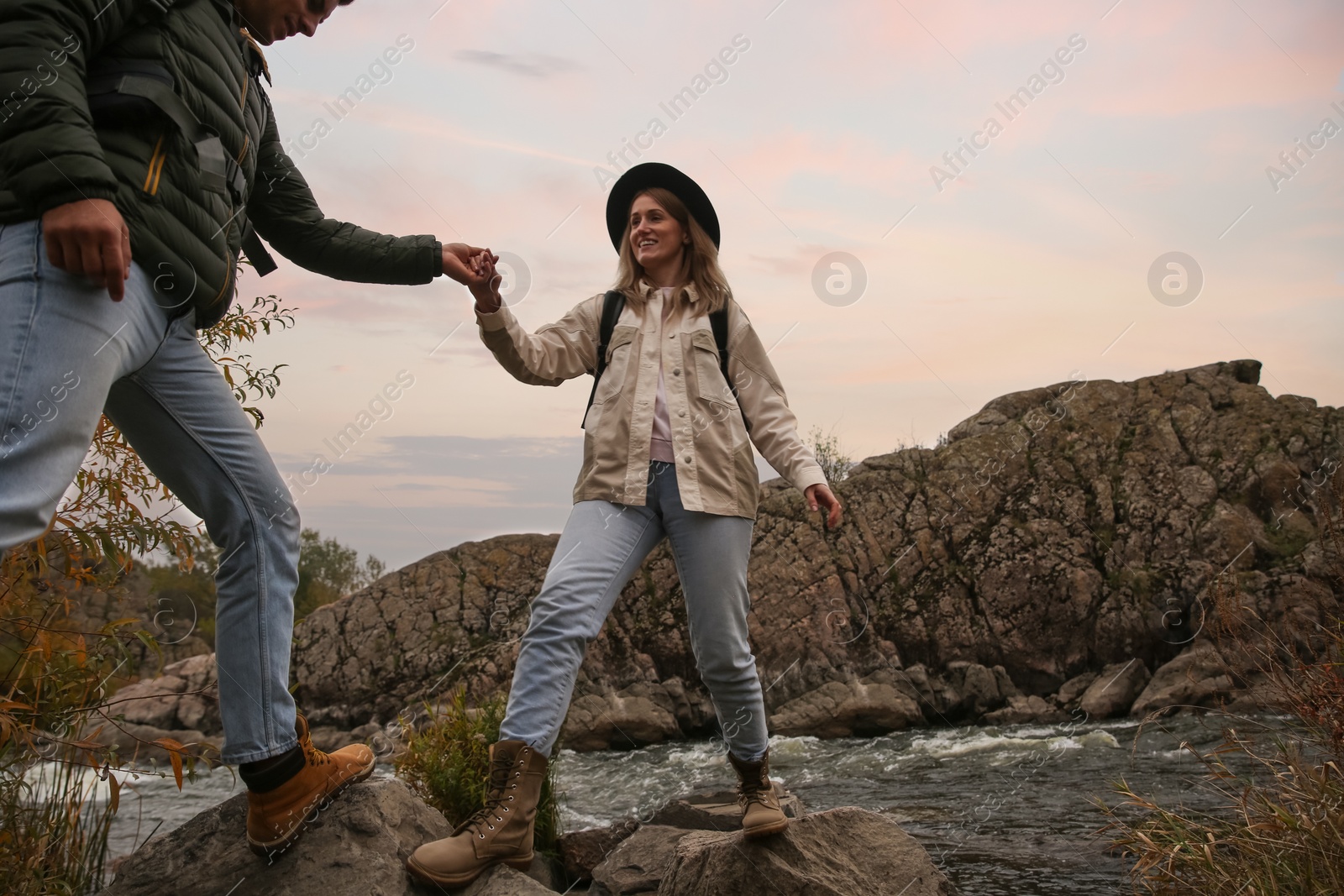 Photo of Group of friends with backpacks crossing mountain river on autumn day