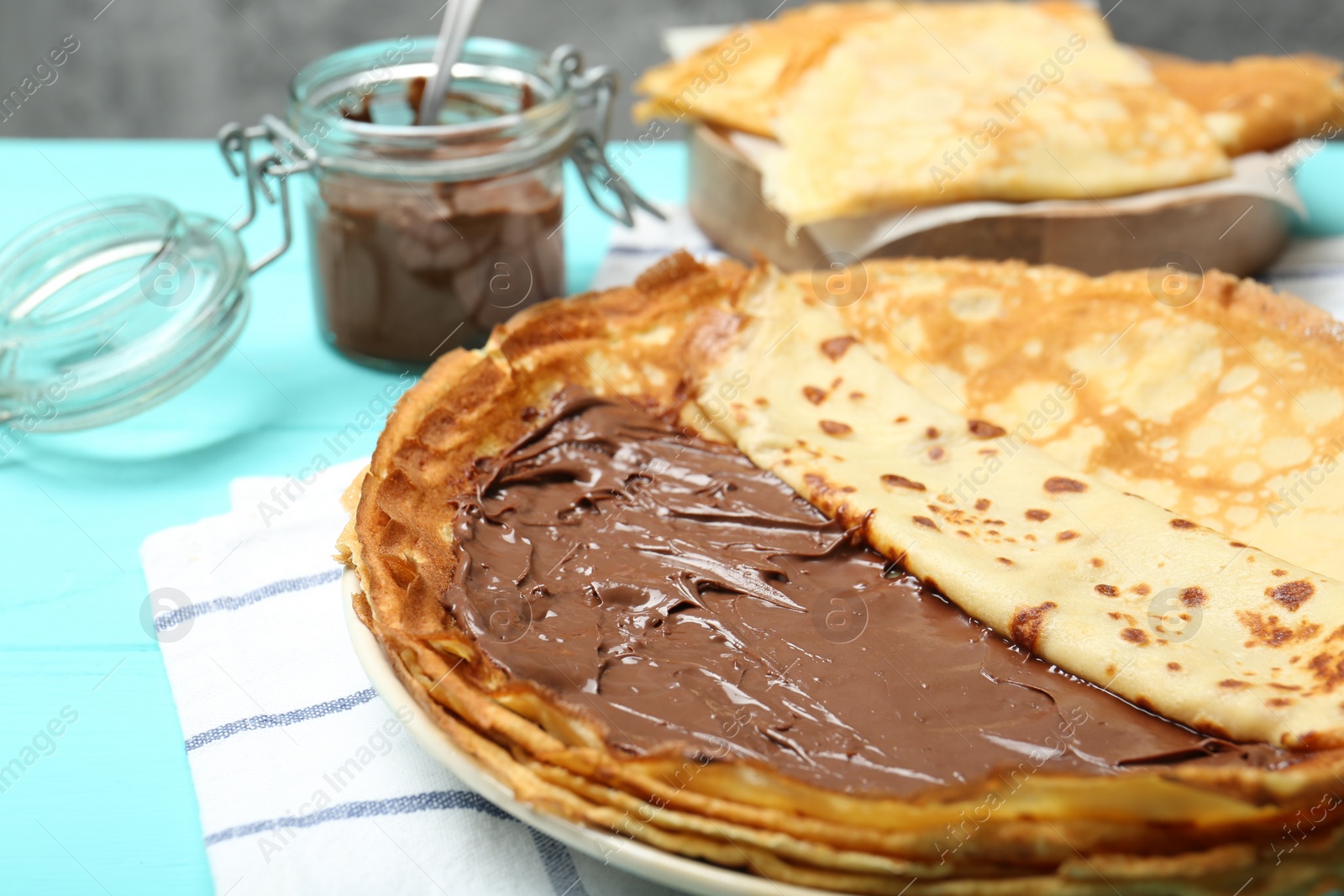 Photo of Tasty crepes with chocolate paste served on turquoise wooden table, closeup