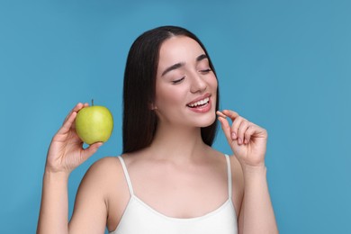 Photo of Beautiful young woman with vitamin pill and apple on light blue background