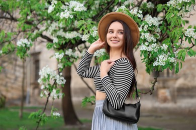 Photo of Beautiful woman in hat near blossoming tree on spring day