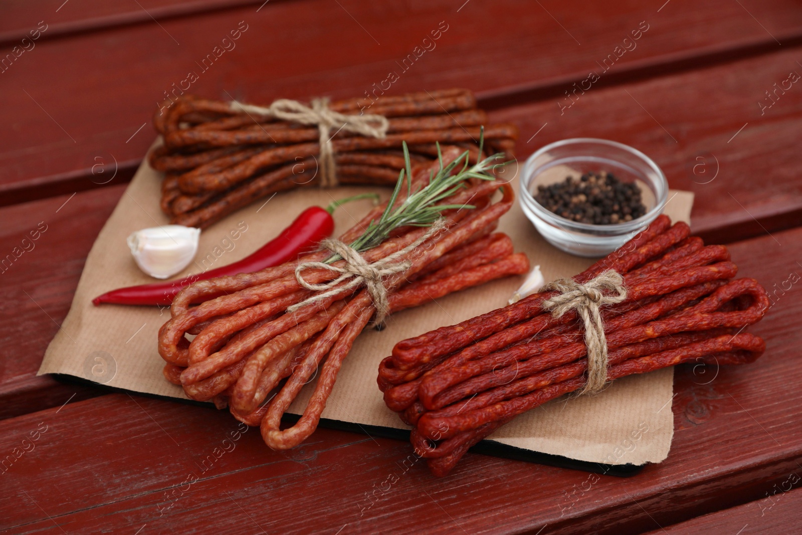 Photo of Bundles of delicious kabanosy with rosemary, peppercorn, garlic and chilli on wooden table