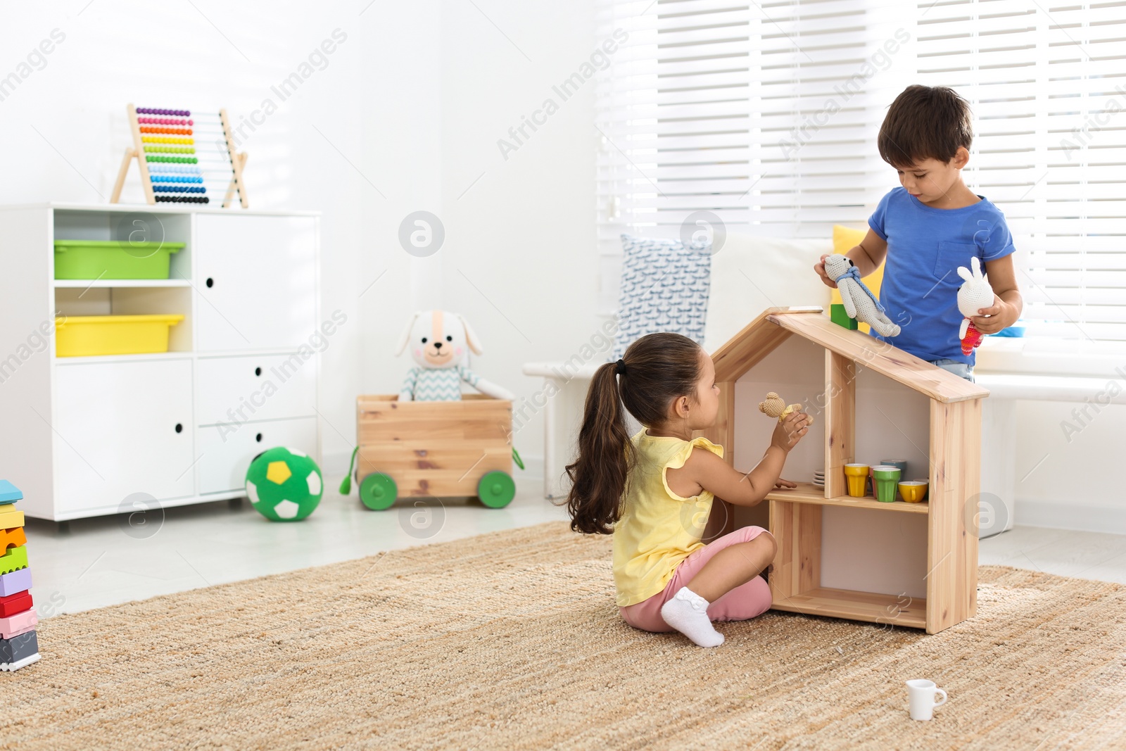 Photo of Cute little children playing with toys near wooden house on floor at home, space for text