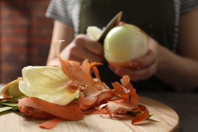 Photo of Woman peeling fresh onion at table indoors, selective focus