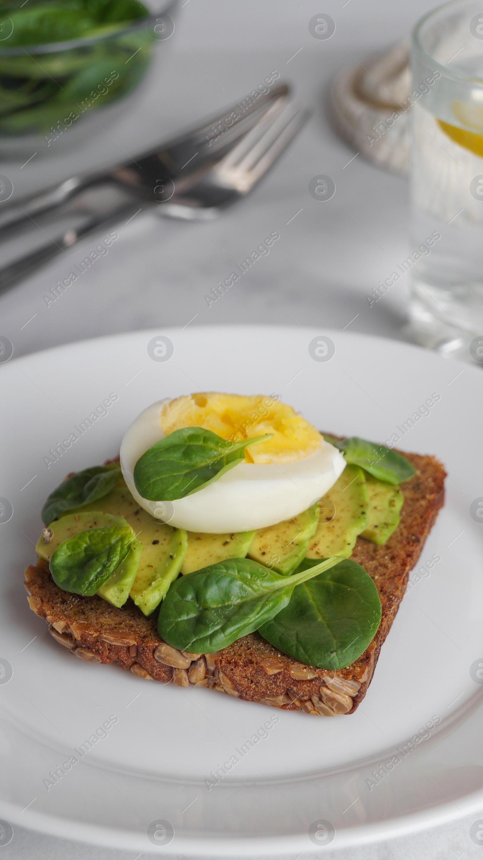 Photo of Tasty sandwich with boiled egg, avocado and spinach on white marble table, closeup