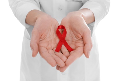 Doctor holding red awareness ribbon on white background, closeup. World AIDS disease day