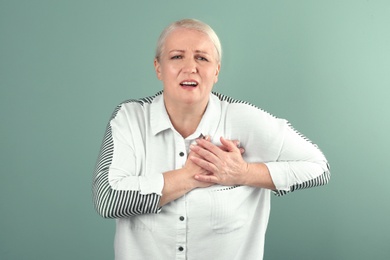 Mature woman having heart attack on color background