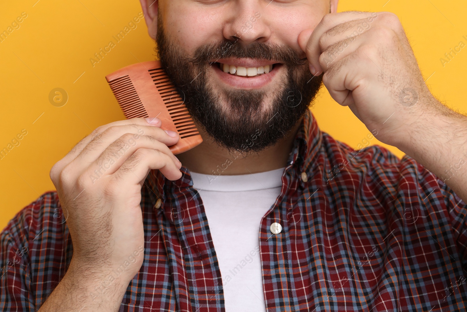 Photo of Handsome young man combing beard on yellow background, closeup