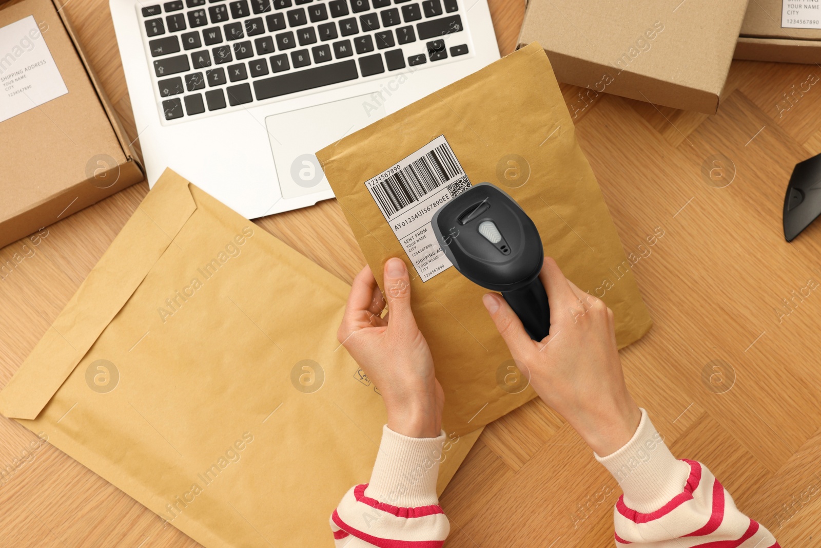 Photo of Woman with scanner reading parcel barcode at wooden table, top view. Online store