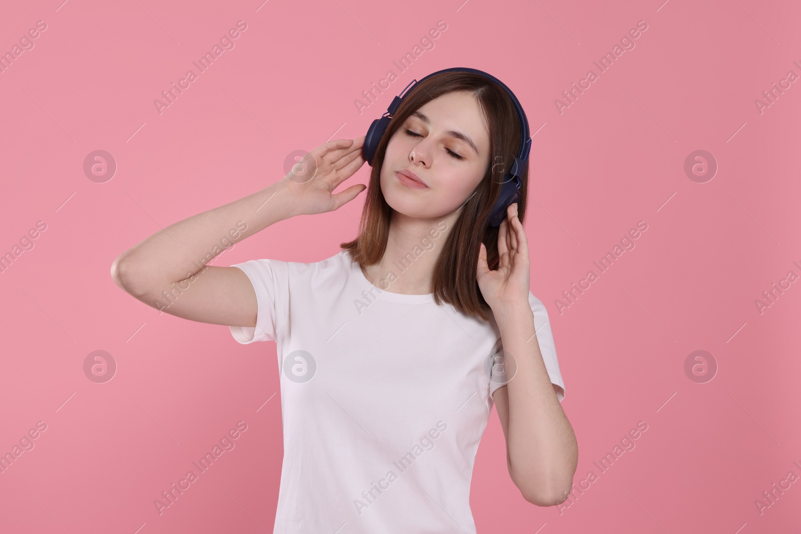 Photo of Cute teenage girl listening music with headphones on pink background