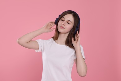 Cute teenage girl listening music with headphones on pink background