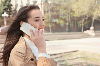 Photo of Young woman talking by phone outdoors on sunny day