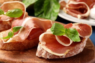 Photo of Tasty sandwiches with cured ham and basil leaves on wooden board, closeup