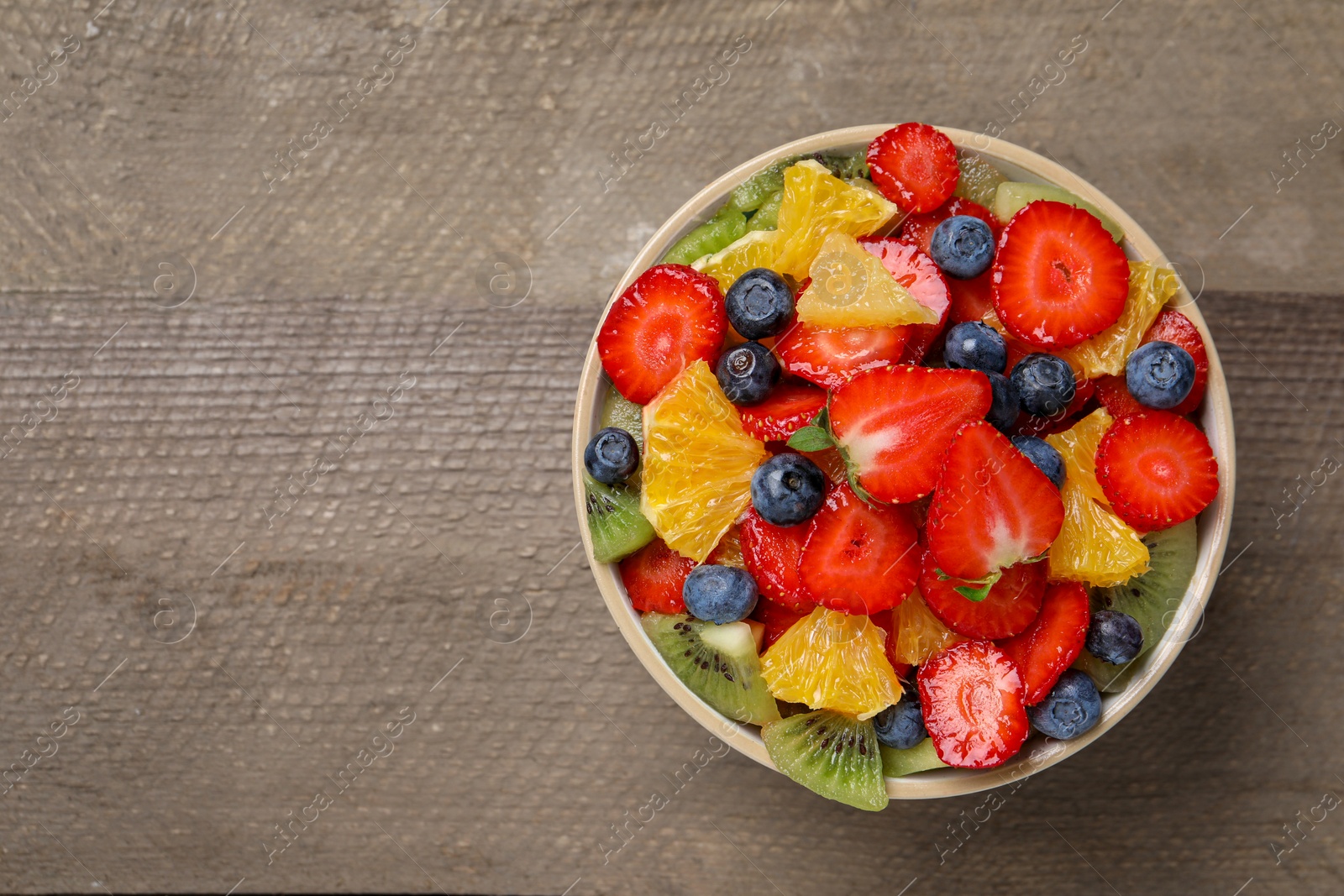 Photo of Delicious fresh fruit salad in bowl on wooden table, top view. Space for text