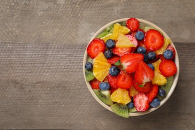 Delicious fresh fruit salad in bowl on wooden table, top view. Space for text