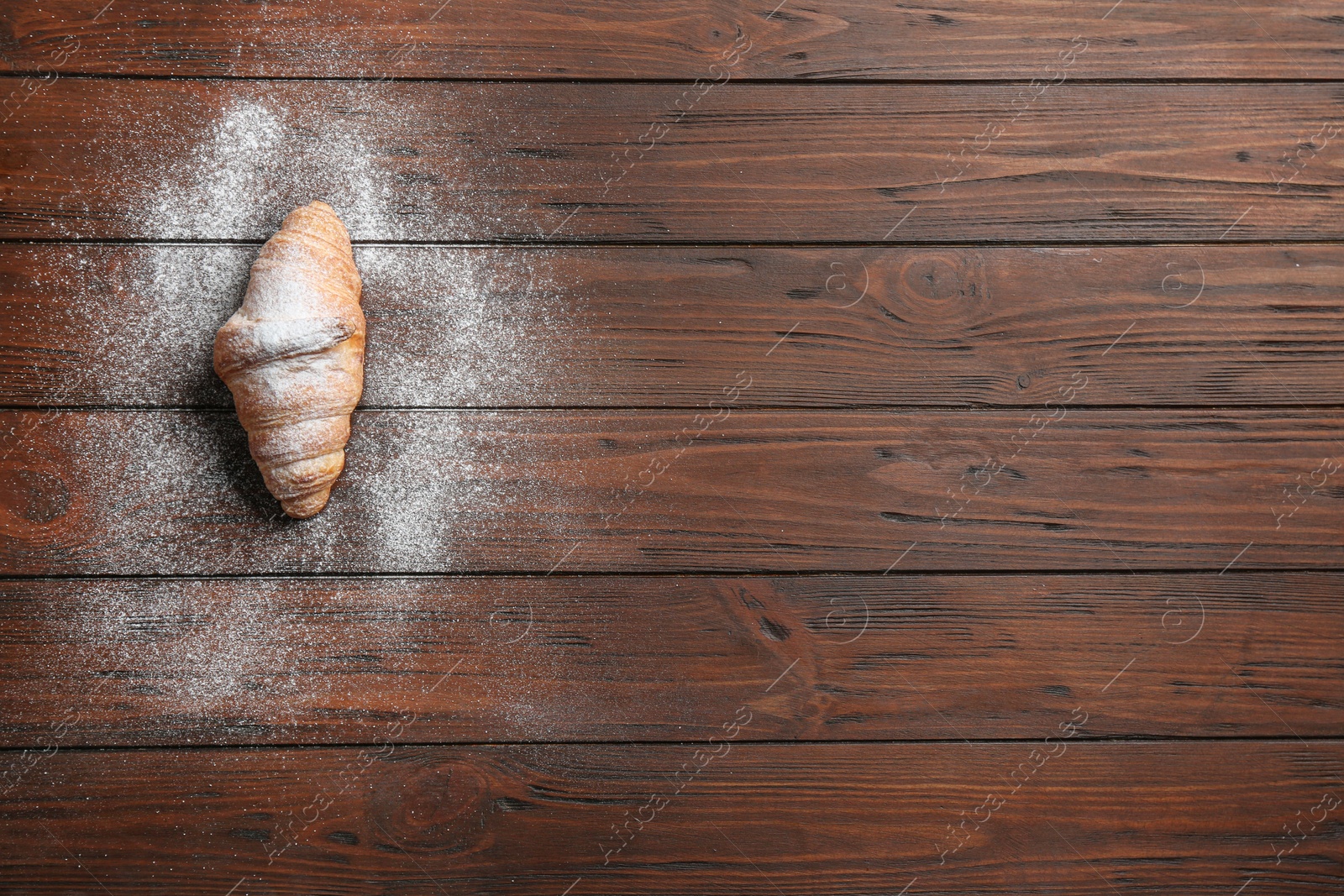 Photo of Tasty croissant with powdered sugar and space for text on wooden background, top view. French pastry