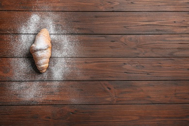 Photo of Tasty croissant with powdered sugar and space for text on wooden background, top view. French pastry