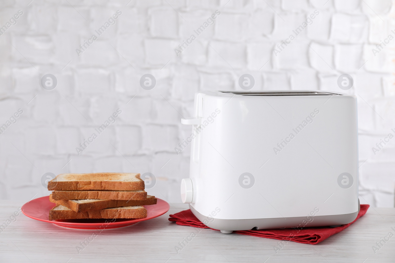 Photo of Modern toaster and slices of bread on white wooden table