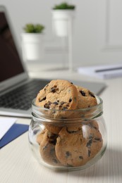 Jar with chocolate chip cookies on white wooden table in office