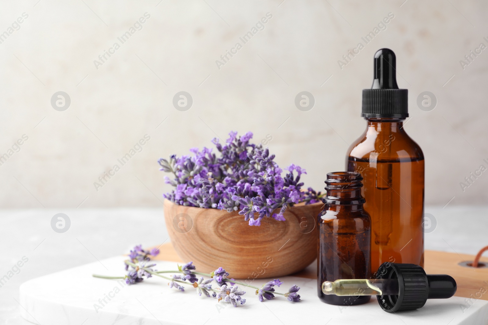 Photo of Bottles with natural essential oil and bowl of lavender flowers on table against light background. Space for text