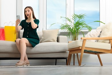 Special Promotion. Emotional young woman looking at smartphone on sofa indoors