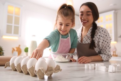 Photo of Mother and daughter making dough at table in kitchen, focus on hand