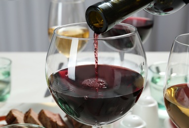 Pouring red wine into glass on table, closeup