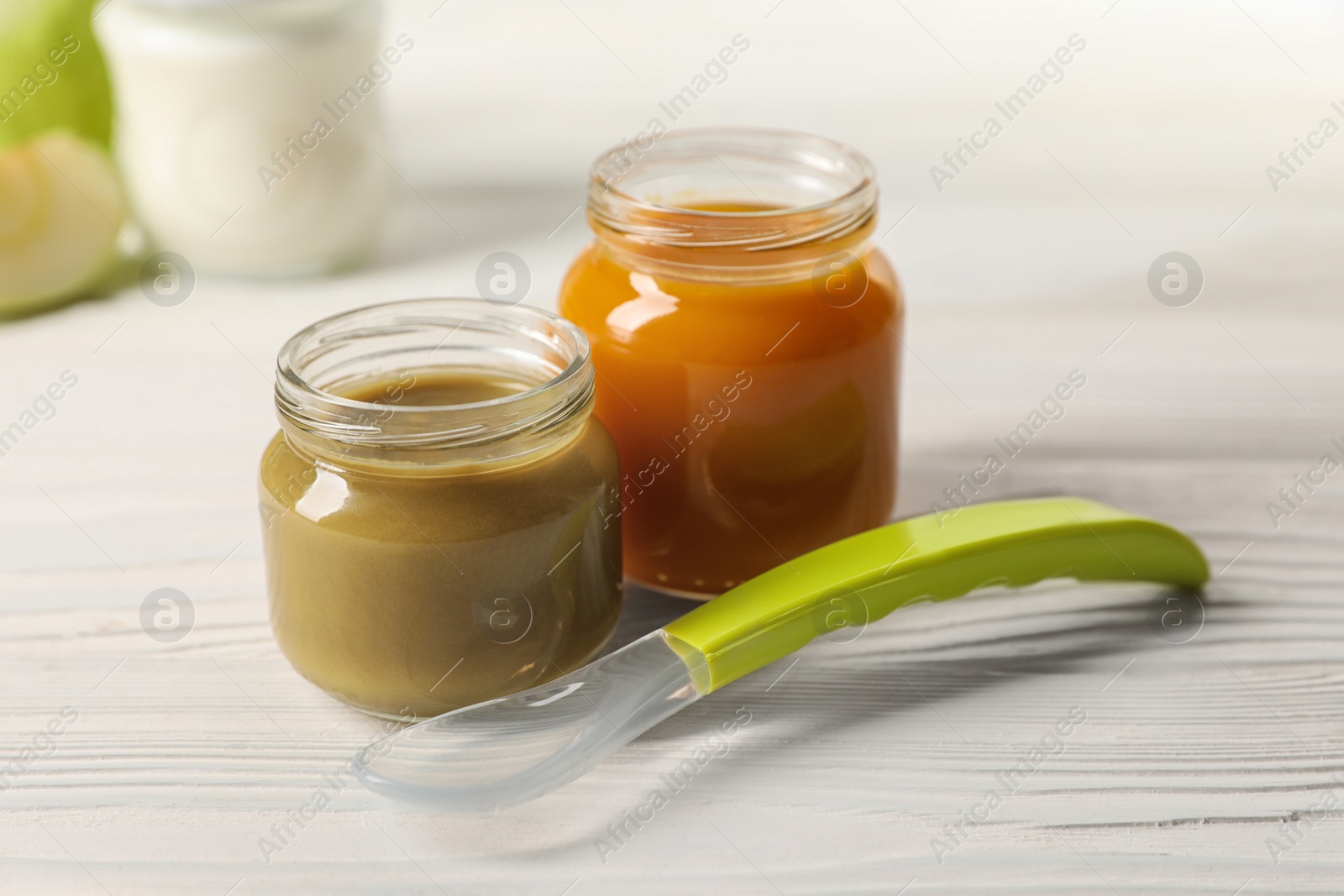 Photo of Jars with healthy baby food and spoon on white wooden table