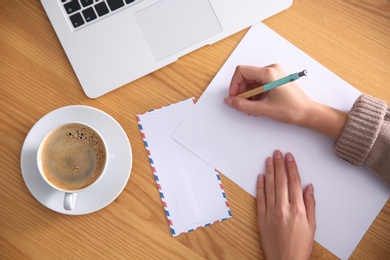 Woman writing letter at wooden table, top view