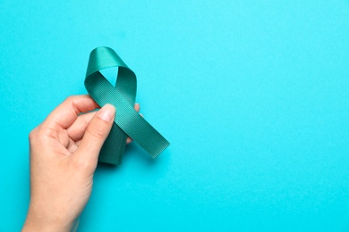 Photo of Woman holding teal awareness ribbon on light blue background, top view with space for text. Symbol of social and medical issues