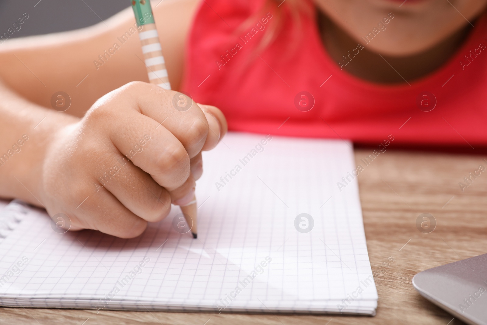 Photo of Cute little girl doing homework at table, closeup