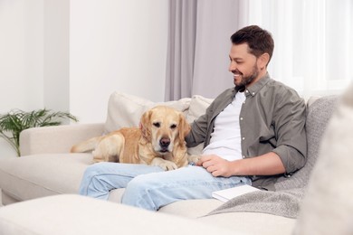 Photo of Happy man sitting on sofa with his cute Labrador Retriever at home