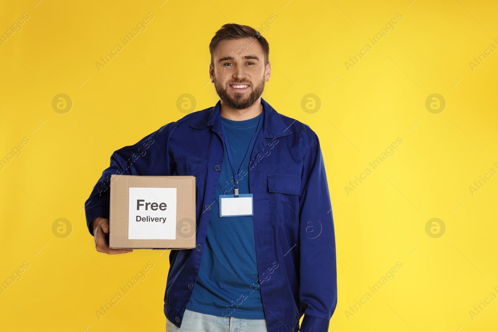 Photo of Male courier holding parcel with sticker Free Delivery on yellow background