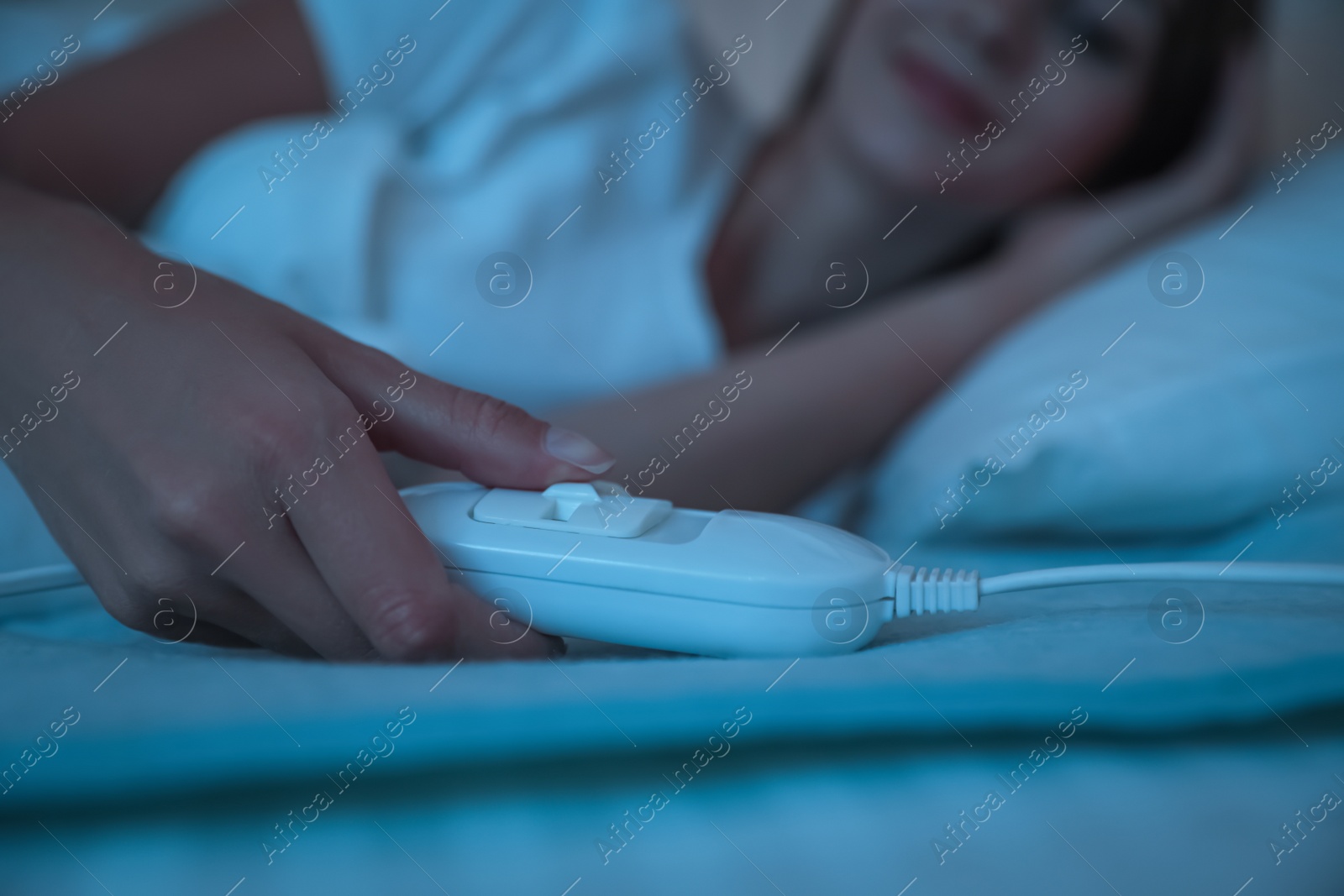 Photo of Young woman in bed with electric heating pad, focus on cable