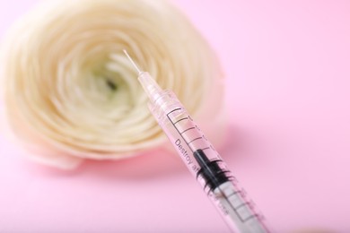 Cosmetology. Medical syringe and ranunculus flower on pink background, closeup